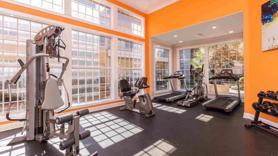 a gym room with orange walls and windows at The Westmount at Three Fountains